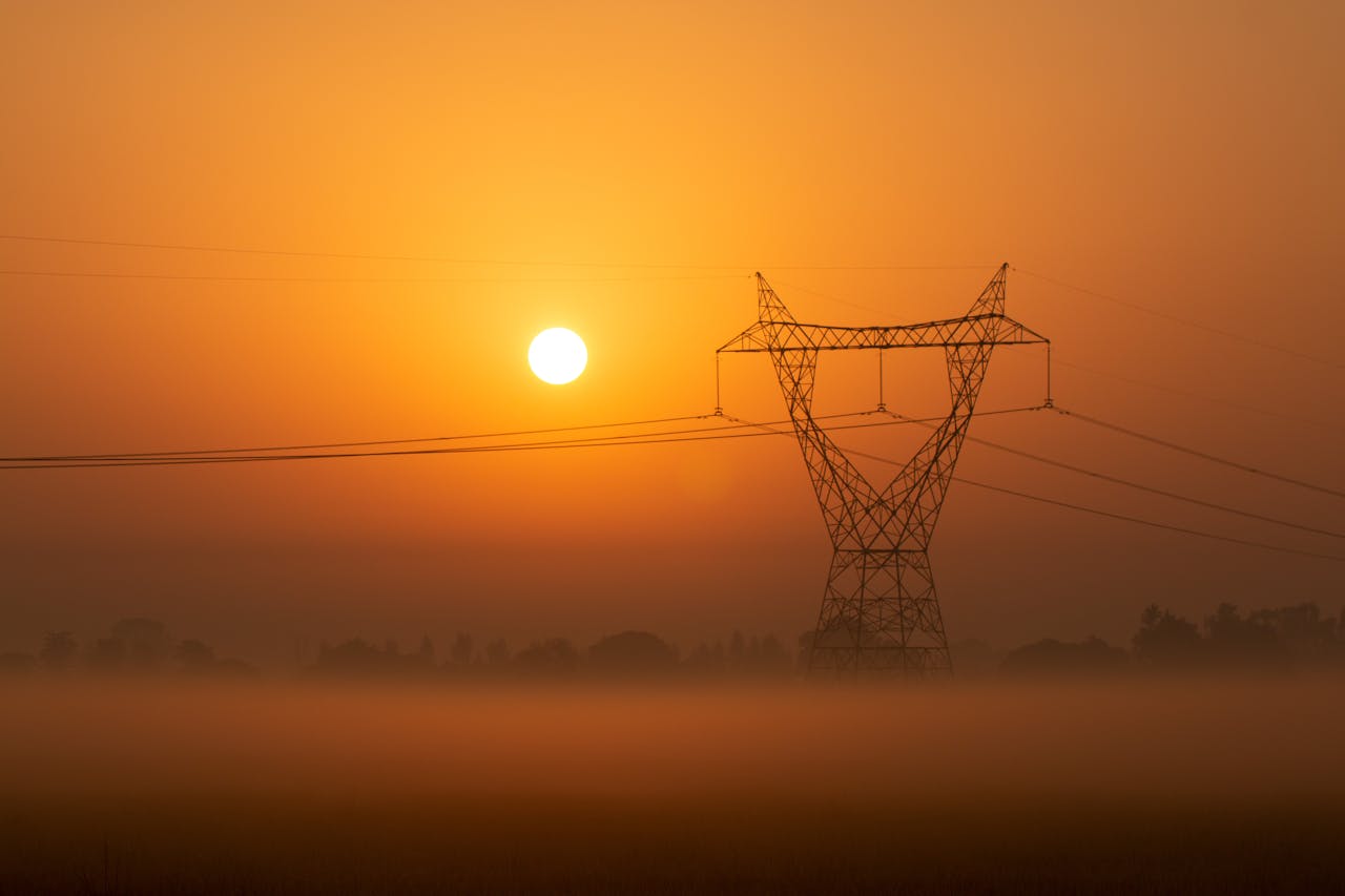 Silhouette of a power line tower at sunset in a foggy landscape, creating a serene scene.